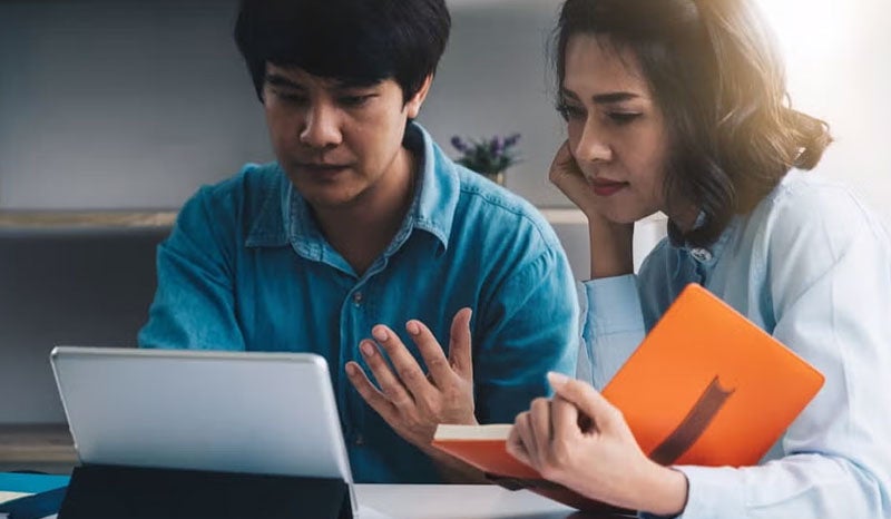 Two people working together on a laptop, one of them gesturing.