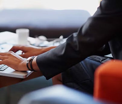 Close-up of a person in a business suit typing on a laptop at a desk.
