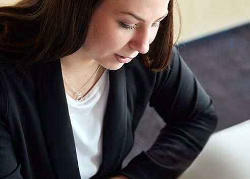 A female young professional dressed in a black blazer works quietly while seated in an office room.