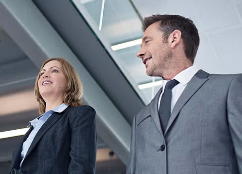 A man and a woman in business suits walking together, discussing something.