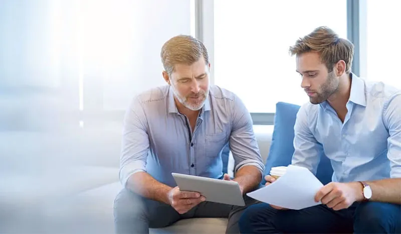 Two professionals discussing over a tablet and a document in a modern office setting.