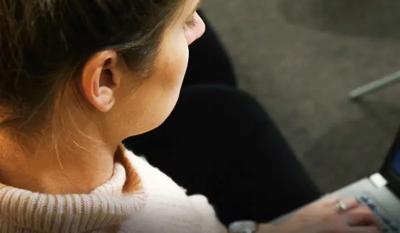 A woman working intently on her laptop in an office setting.